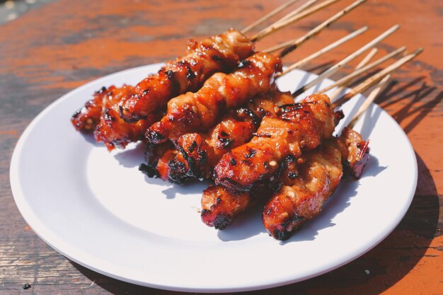 Chicken Satay or Chicken skin satay with red spices on white plate isolated on wooden tables