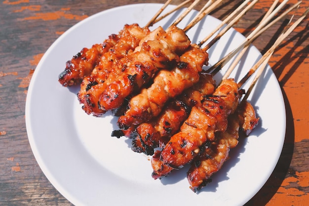 Chicken Satay or Chicken skin satay with red spices on white plate isolated on wooden tables