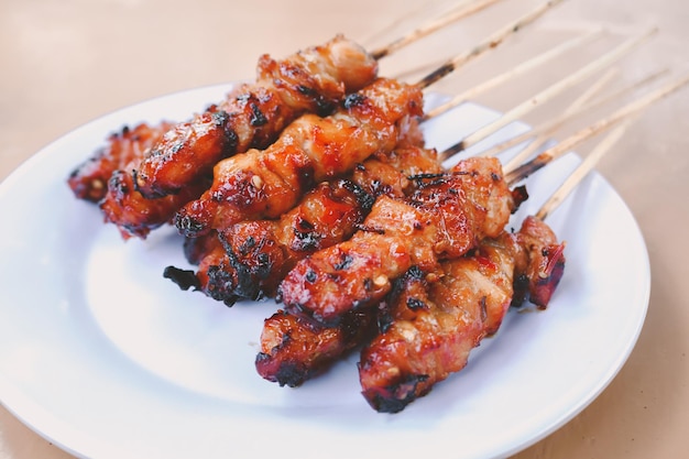 Chicken Satay or Chicken skin satay with red spices on white plate isolated on wooden tables