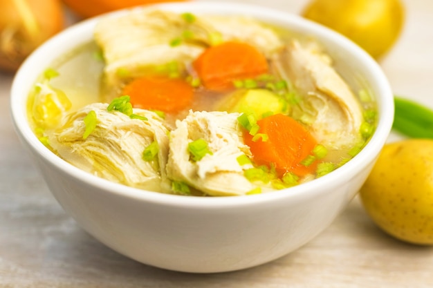 Chicken Soup stew broth and vegetables in white bowl on old rustic wooden cutting board. Close up. Selective focus. Copy space