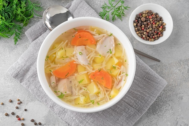 Chicken soup with noodles and vegetables in white bowl on a gray concrete background