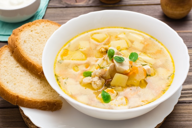 chicken soup with potatoes and herbs in a white bowl on a wooden table