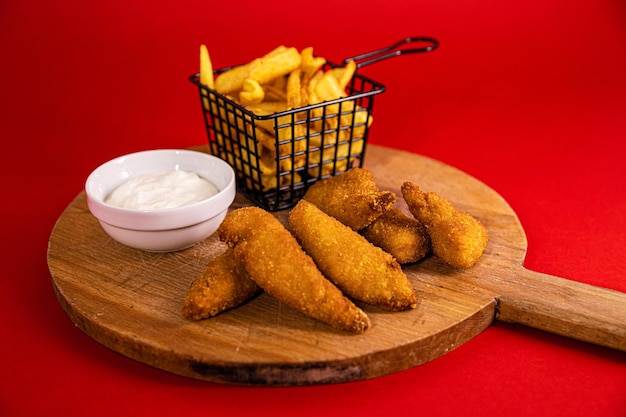 Chicken sticks and french fries served with mayonnaise on a wooden board