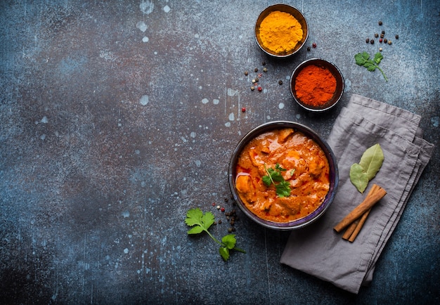 Chicken tikka masala with spicy curry meat served in rustic ceramic bowl, popular Indian dish, on concrete background, top view and space for text