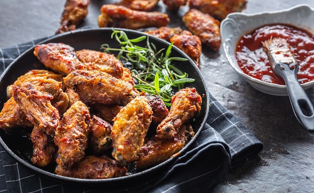 Chicken wings barbeque in a cast iron baking dish with BBQ sauce and rosemary.