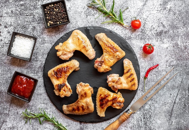 Chicken wings on a black plate with spices and herbs on a gray background.