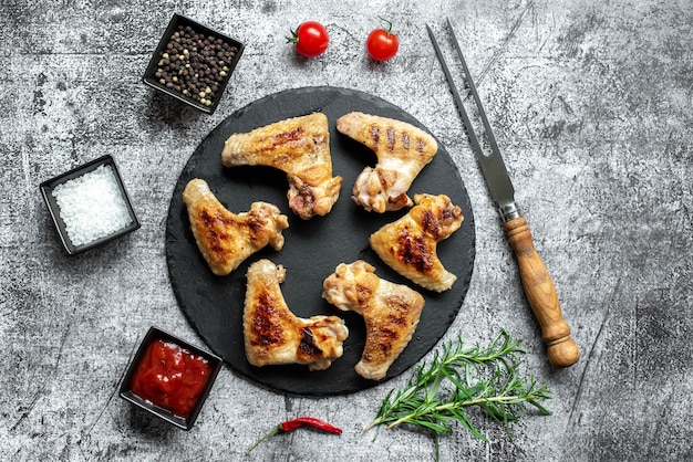 Chicken wings on a black plate with spices and sauces.