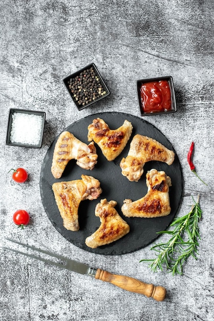 Chicken wings on a black plate with spices and tomatoes.