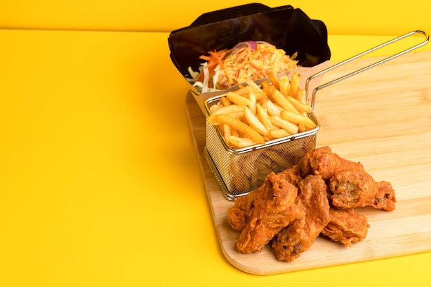 Chicken wings with salad and potatoes yellow background side view