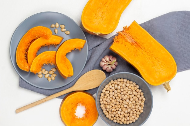 Chickpeas in gray bowl Two halves of pumpkin wooden spoon and garlic on gray napkin