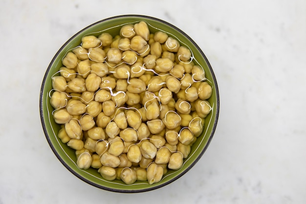 Chickpeas soaked in water, in bowl, on marble table. Concept of healthy eating, veganism, vegetarianism, meat and egg replacement. Prepare chickpeas before making hummus and other legume dishes.