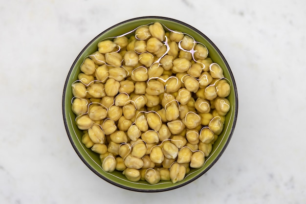 Chickpeas soaked in water, in bowl, on marble table. Concept of healthy eating, veganism, vegetarianism, meat and egg replacement. Prepare chickpeas before making hummus and other legume dishes.