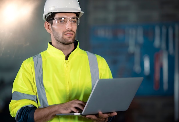 Chief Engineer in the Hard Hat Walks Through Light Modern Factory While Holding Laptop.