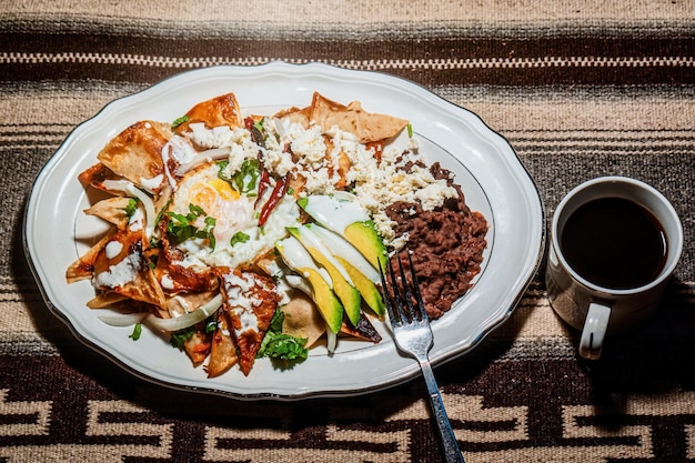 Chilaquiles Mexican food with in red sauce cheese cream chili peppers on vintage background and coffee