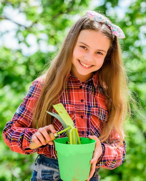 Child adorable kid hold flower pot and hoe gardening tool Gardening is peaceful meditative occupation Gardening classes Ecology education Little girl planting plants Planting season Garden care