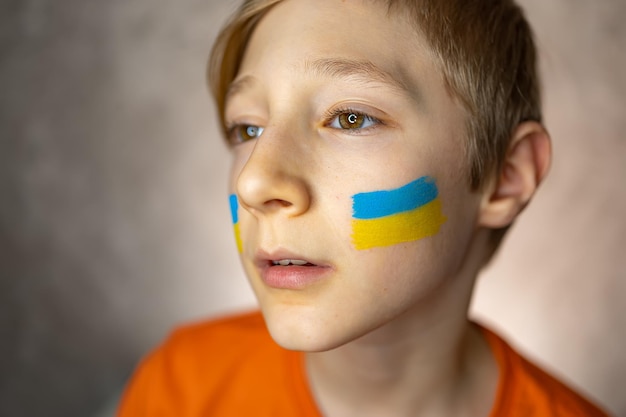 A child against the war a tearful boy with a painted flag of Ukraine on his cheeks looks with pity at the camera