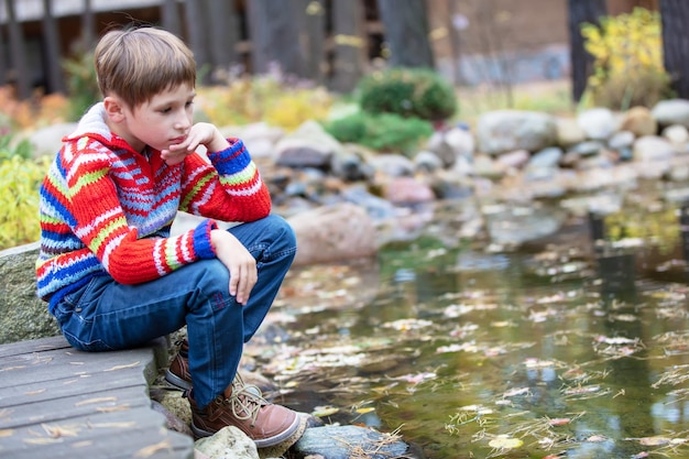 Child on an autumn walk Sad boy by the lake