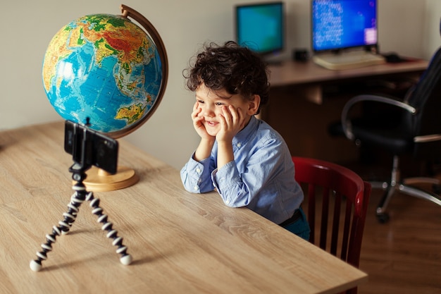 A child blogger shoots a video on a smartphone on a tripod the boy poses on a smartphone camera shoo...