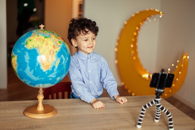 A child blogger shoots a video on a smartphone on a tripod the boy poses on a smartphone camera shoo...