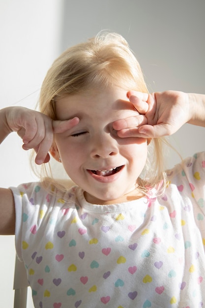 Child blonde girl waking up in the morning will rub her eyes under the rays of the sun