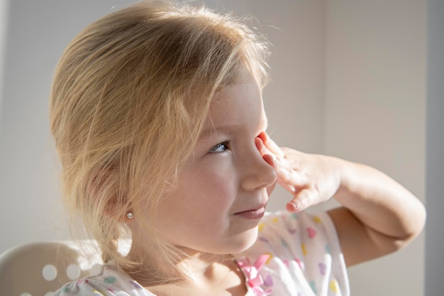 Child blonde girl waking up in the morning will rub her eyes under the rays of the sun