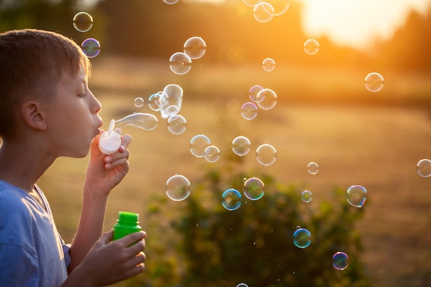 Child blowing soap bubbles on a summer day at sunset nature.