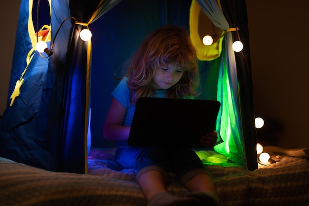 Child boy lying in bed and watching laptop at night little hacker young programmer