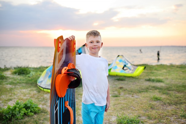 Child boy with a board for swimming or surfing smiling on the sea