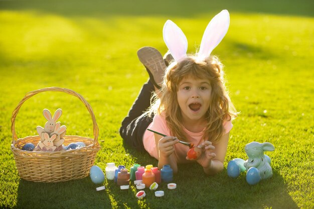 Child boy with easter eggs and bunny ears painting eggs outdoor cute kid having happy easter in park