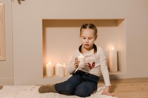 A child by the fireplace holds a burning candle