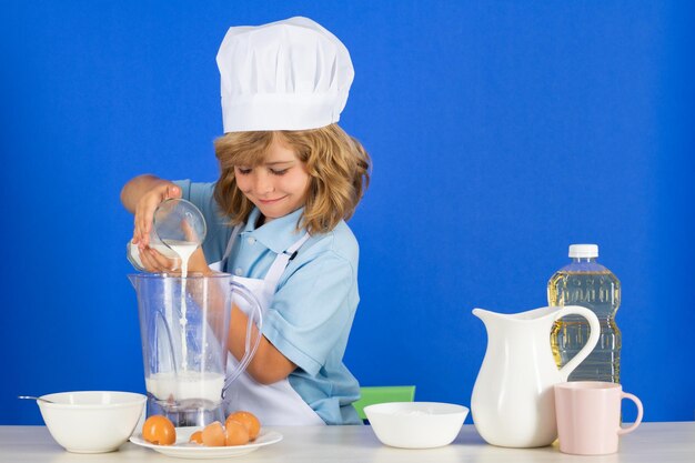 Child chef cook prepares food in isolated blue studio background kids cooking teen boy with apron an