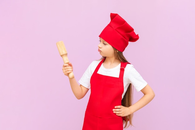 A child chef looks at a wooden rolling pin on an isolated pink background Baking for children