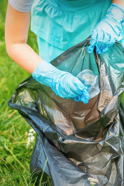 Photo child collects plastic trash from grass throwing garbage in garbage bag in the park