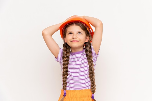 A child in a construction helmet holds his head with his hands A beautiful little girl is getting ready for repairs on a white isolated background