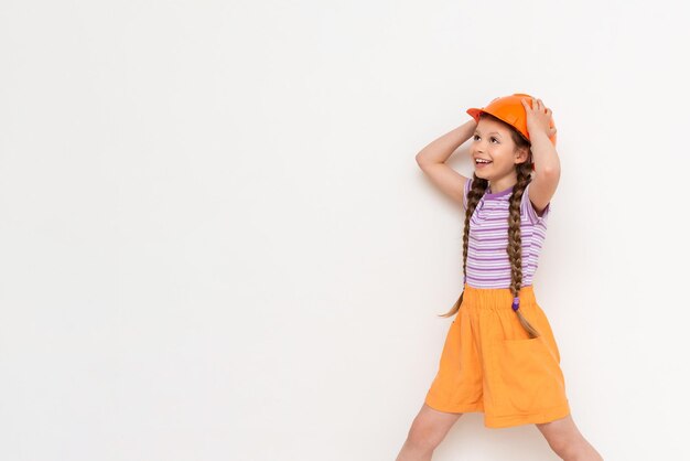 A child in a construction helmet holds his head with his hands A beautiful little girl is getting ready for repairs on a white isolated background