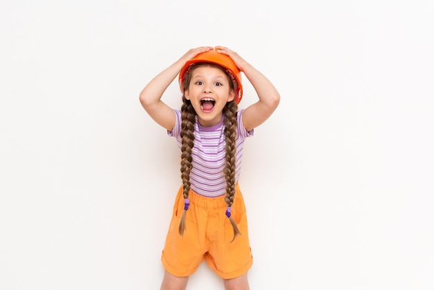 A child in a construction helmet holds his head with his hands A beautiful little girl is getting ready for repairs on a white isolated background