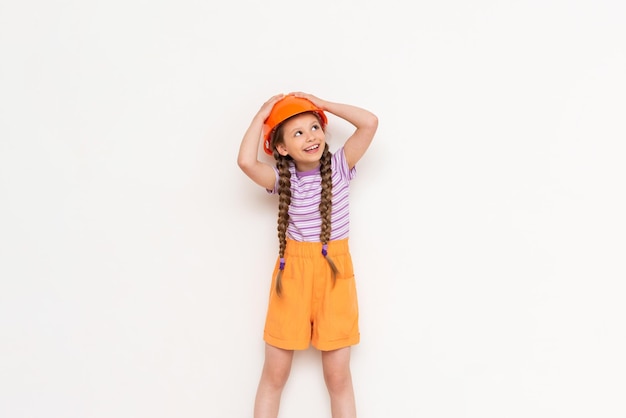 A child in a construction helmet holds his head with his hands A beautiful little girl is getting ready for repairs on a white isolated background