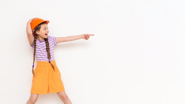 A child in a construction helmet points to your advertisement A little girl with pigtails on a white isolated background Profession in the construction industry