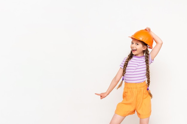 A child in a construction helmet points to your advertisement A little girl with pigtails on a white isolated background Profession in the construction industry