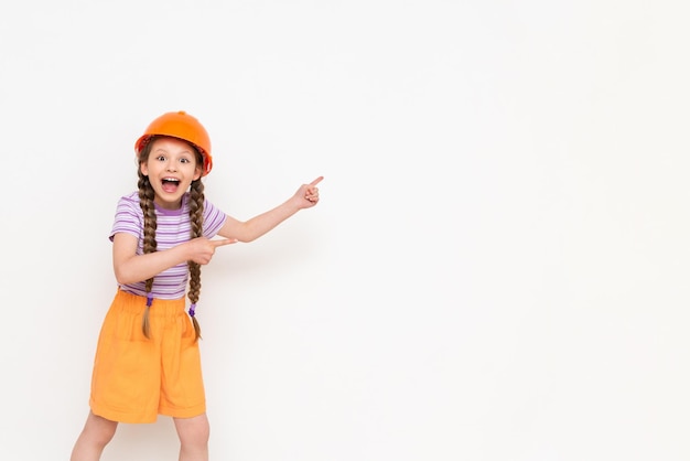 A child in a construction helmet points to your advertisement A little girl with pigtails on a white isolated background Profession in the construction industry