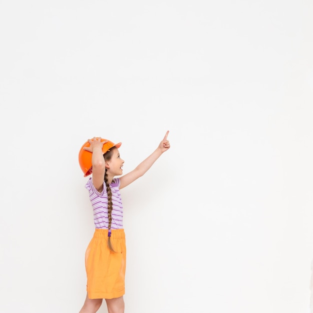 A child in a construction helmet points to your advertisement A little girl with pigtails on a white isolated background Profession in the construction industry