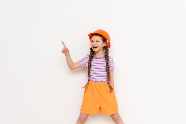 A child in a construction helmet points to your advertisement A little girl with pigtails on a white isolated background Profession in the construction industry