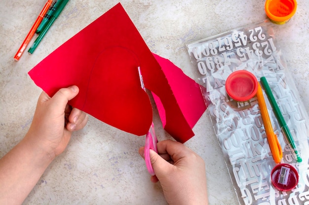 Child cuts out big red heart. St. Valentines day theme. Crafts concept. Kid makes art project