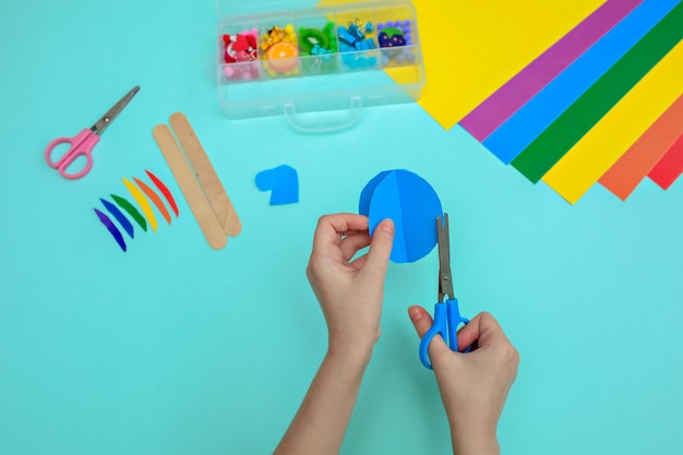 Child cutting colored red paper with scissors at the table