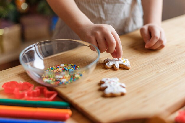 The child decorates christmas gingerbread cookies on a wooden table.