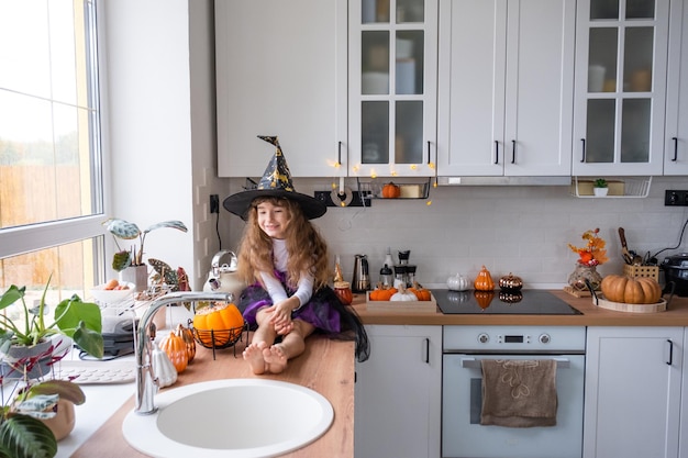 Child decorates the kitchen in home for Halloween Girl in a witch costume plays with the decor for the holiday bats jack lantern pumpkins Autumn comfort in house Scandistyle kitchen loft