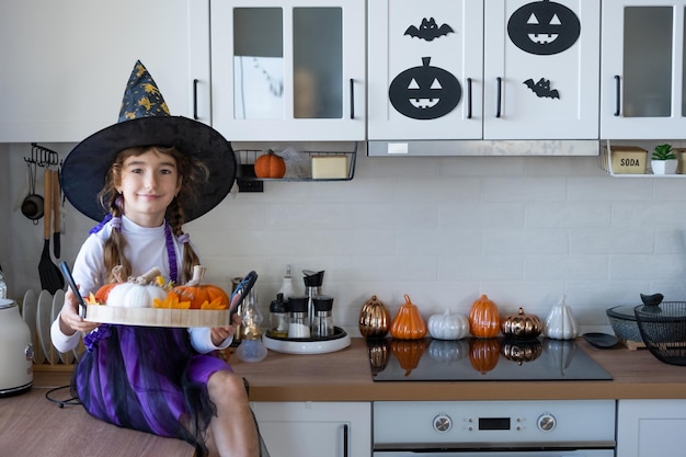 Child decorates the kitchen in home for Halloween Girl in a witch costume plays with the decor for the holiday bats jack lantern pumpkins Autumn comfort in house Scandistyle kitchen loft