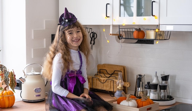 Child decorates the kitchen in home for Halloween Girl in a witch costume plays with the decor for the holiday bats jack lantern pumpkins Autumn comfort in house Scandistyle kitchen loft