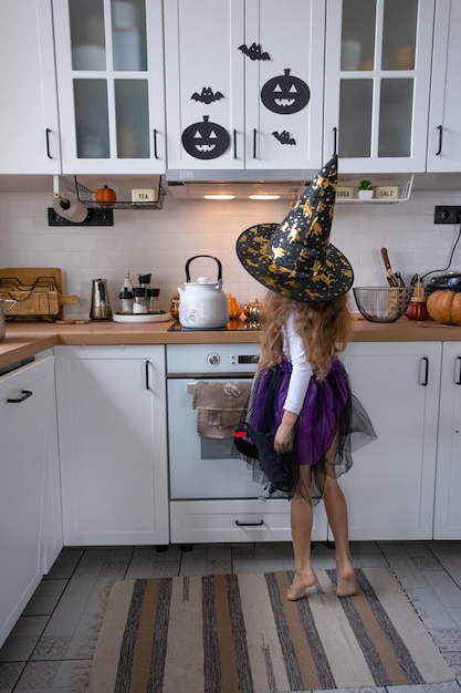 Child decorates the kitchen in home for Halloween Girl in a witch costume plays with the decor for the holiday bats jack lantern pumpkins Autumn comfort in house Scandistyle kitchen loft