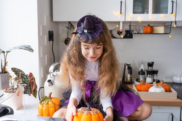 Child decorates the kitchen in home for Halloween Girl in a witch costume plays with the decor for the holiday bats jack lantern pumpkins Autumn comfort in house Scandistyle kitchen loft